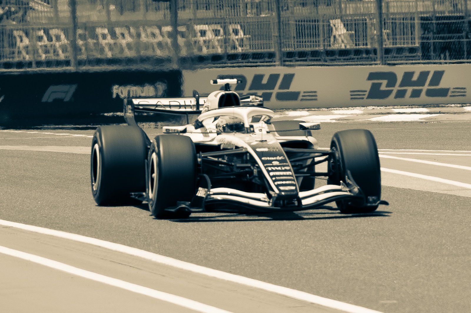 A Formula 1 car speeds past DHL barriers on track.